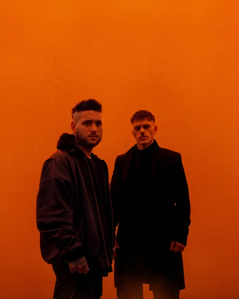 El dúo sobre un fondo naranja con humo